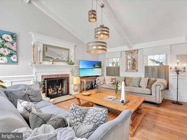 living area featuring high vaulted ceiling, a notable chandelier, a brick fireplace, beam ceiling, and light wood finished floors