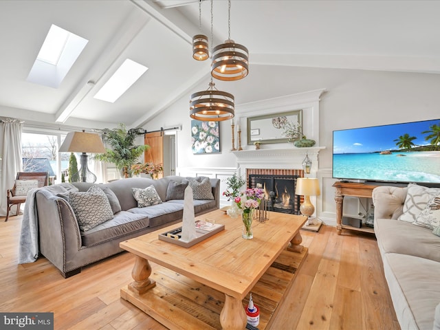 living area with lofted ceiling with skylight, a brick fireplace, light wood finished floors, and a barn door