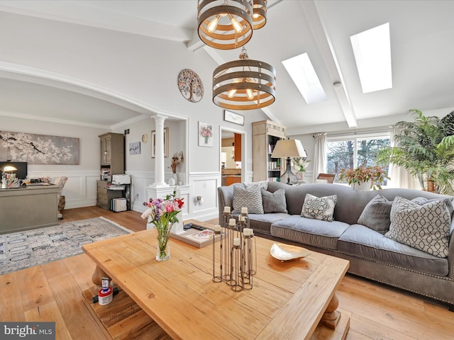 living room featuring lofted ceiling with beams, light wood finished floors, a wainscoted wall, and ornate columns