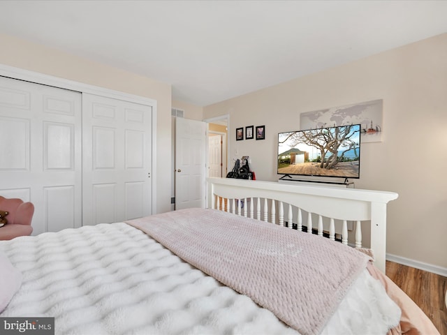 bedroom featuring baseboards, visible vents, a closet, and wood finished floors