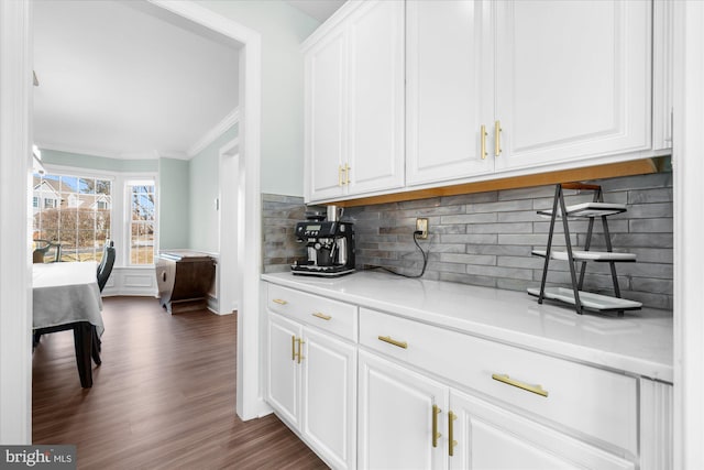 bar with tasteful backsplash, light stone counters, crown molding, white cabinetry, and dark hardwood / wood-style floors