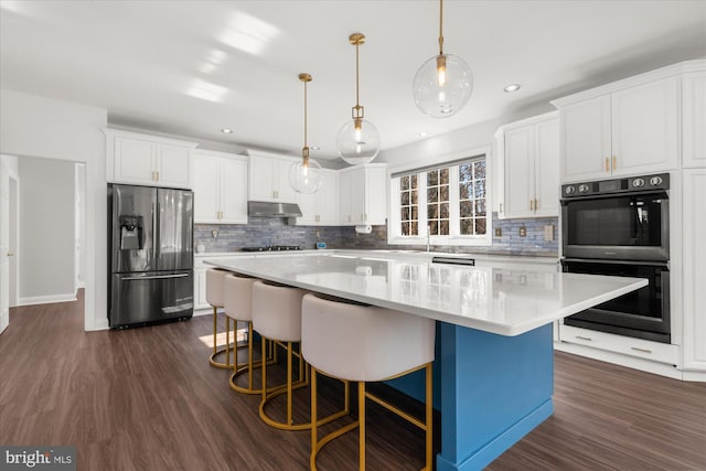 kitchen with hanging light fixtures, double wall oven, white cabinets, a center island, and stainless steel fridge with ice dispenser