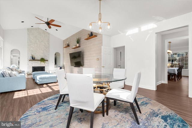 dining space featuring a large fireplace, high vaulted ceiling, dark hardwood / wood-style floors, and ceiling fan with notable chandelier