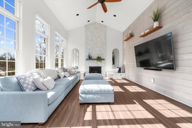 living room with high vaulted ceiling, ceiling fan, a stone fireplace, and hardwood / wood-style flooring