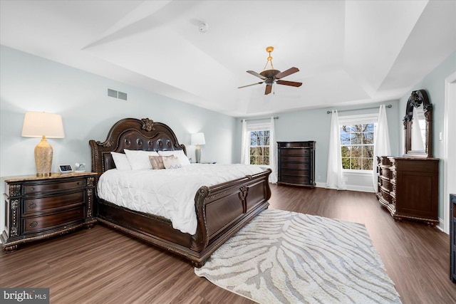 bedroom with a raised ceiling, ceiling fan, and dark hardwood / wood-style floors