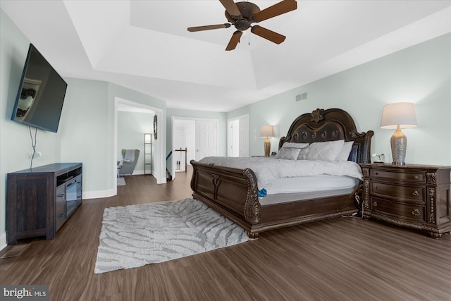 bedroom with a tray ceiling, dark wood-type flooring, and ceiling fan