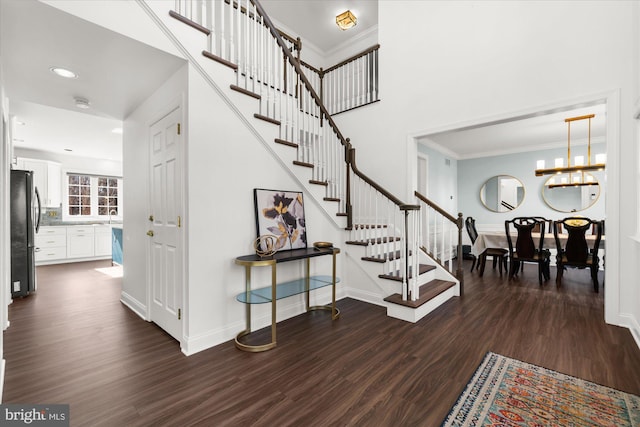 foyer entrance featuring a notable chandelier, sink, dark wood-type flooring, and crown molding