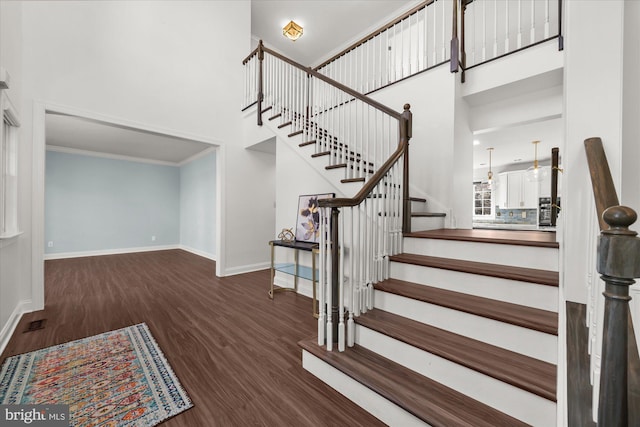 stairway with ornamental molding, a towering ceiling, and wood-type flooring