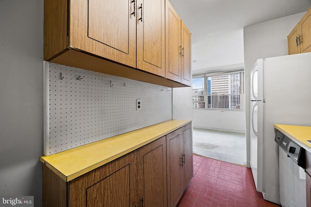 kitchen featuring brick floor, dishwashing machine, light countertops, and freestanding refrigerator