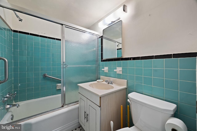 bathroom featuring toilet, shower / bath combination with glass door, tile walls, and vanity