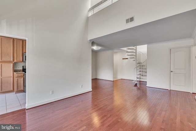 unfurnished living room with visible vents, a high ceiling, hardwood / wood-style floors, and stairway