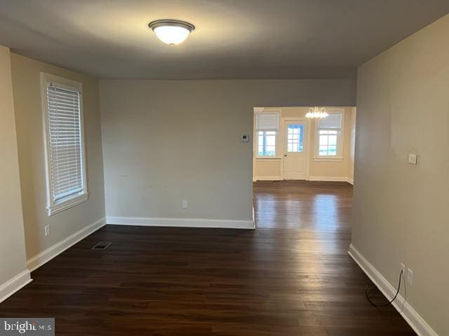 spare room with a chandelier, dark wood-style flooring, visible vents, and baseboards