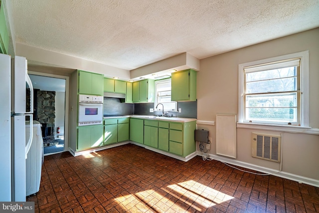 kitchen with visible vents, brick floor, white appliances, green cabinetry, and baseboards