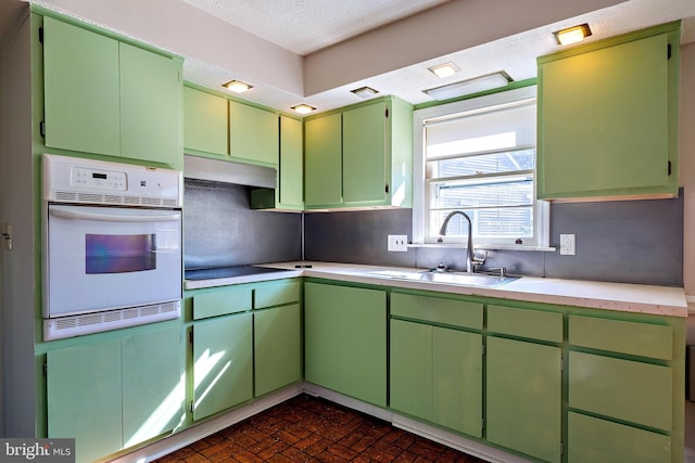 kitchen with under cabinet range hood, a sink, brick floor, light countertops, and white oven