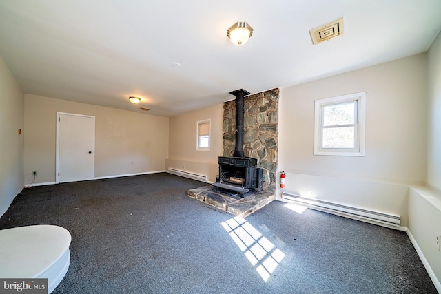 unfurnished living room with a wood stove, a healthy amount of sunlight, and baseboard heating