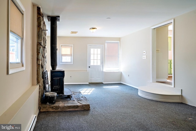 unfurnished living room featuring visible vents, carpet, baseboards, baseboard heating, and a wood stove