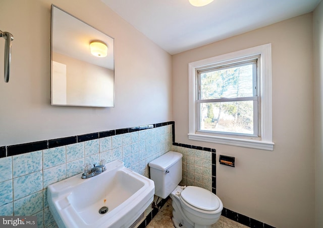 bathroom featuring tile walls, toilet, a wainscoted wall, and a sink