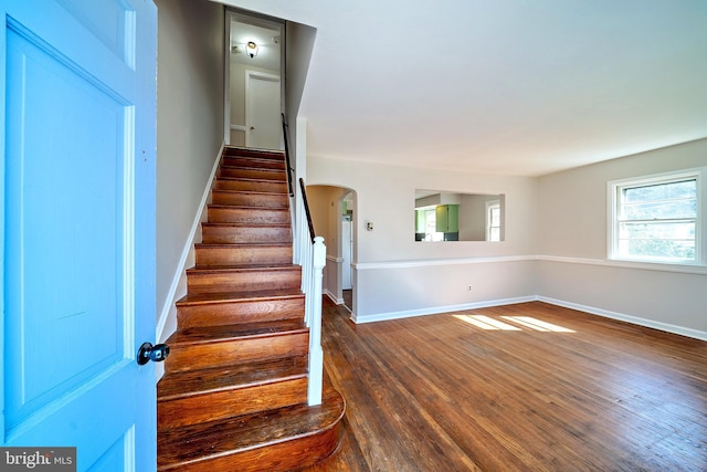 staircase featuring arched walkways, baseboards, and wood finished floors