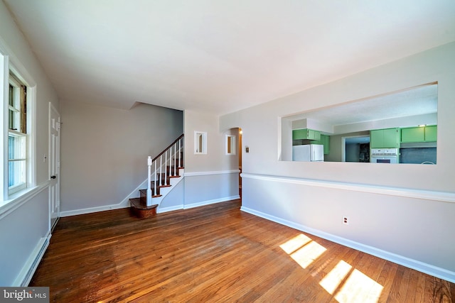 empty room with baseboards, arched walkways, stairs, and hardwood / wood-style flooring