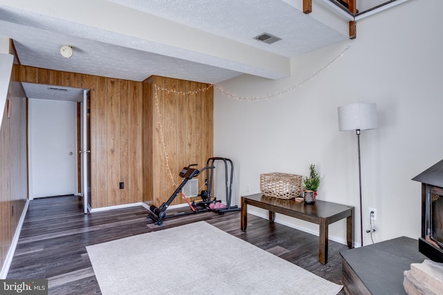 exercise area with wooden walls, a textured ceiling, baseboards, and wood finished floors