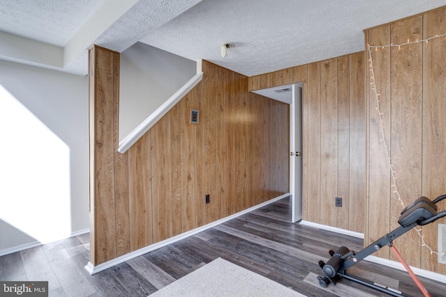 workout area featuring wooden walls, wood finished floors, baseboards, and a textured ceiling