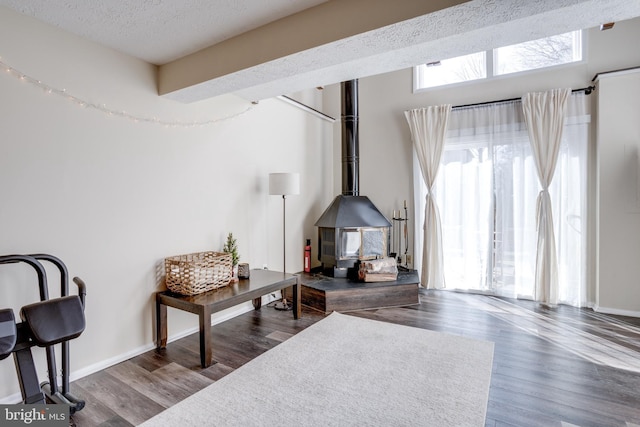 sitting room featuring a wood stove, wood finished floors, baseboards, and a textured ceiling