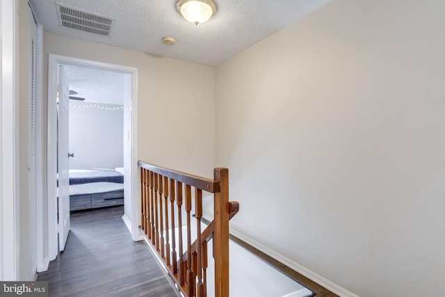 hallway featuring visible vents, baseboards, an upstairs landing, wood finished floors, and a textured ceiling