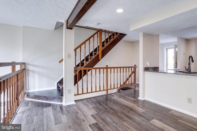 staircase featuring beam ceiling, a textured ceiling, baseboards, and wood finished floors