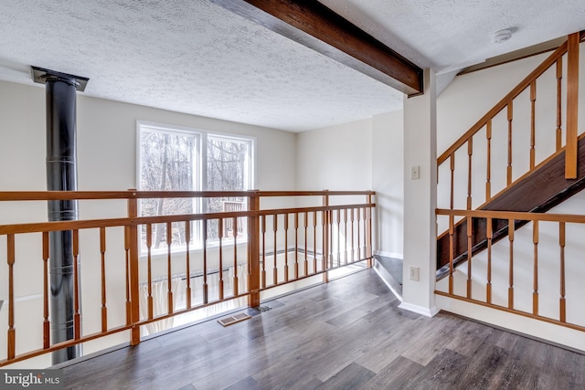 corridor featuring visible vents, beamed ceiling, a textured ceiling, wood finished floors, and baseboards