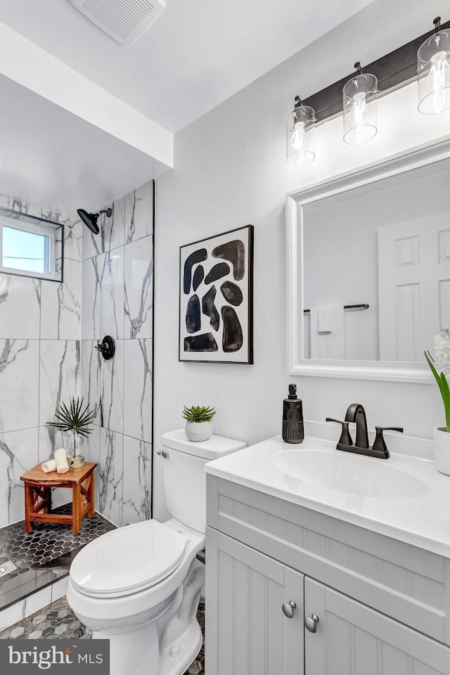 bathroom with a tile shower, vanity, and toilet