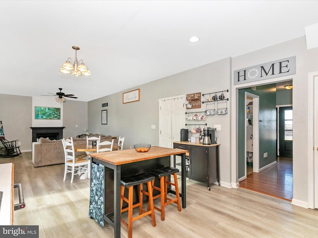 dining area featuring baseboards, a fireplace, light wood finished floors, and ceiling fan with notable chandelier