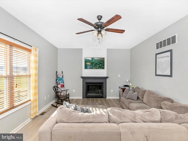 living room with light wood finished floors, a glass covered fireplace, visible vents, and baseboards