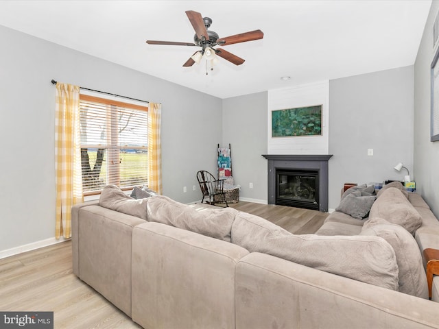 living room featuring light wood-type flooring, baseboards, and a glass covered fireplace