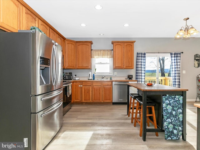 kitchen featuring light wood-style flooring, brown cabinets, stainless steel appliances, a sink, and recessed lighting