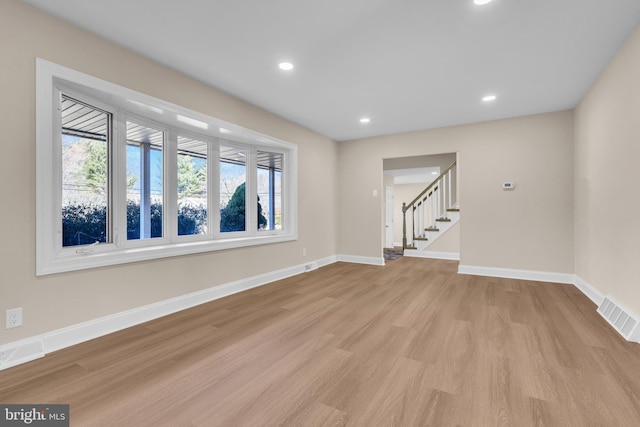 empty room featuring baseboards, visible vents, stairway, and light wood finished floors