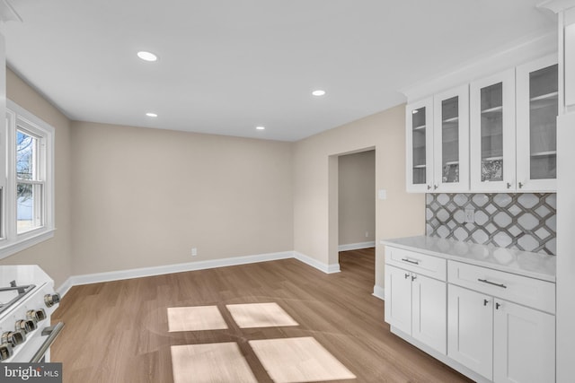 interior space featuring white gas range, light countertops, decorative backsplash, glass insert cabinets, and baseboards