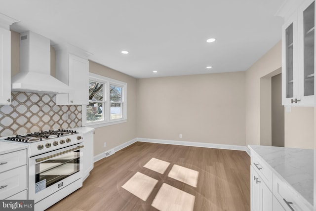 kitchen with white cabinetry, baseboards, wall chimney exhaust hood, tasteful backsplash, and gas range gas stove