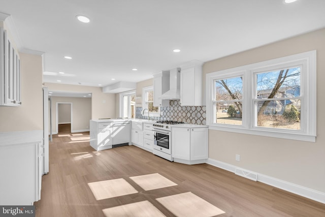 kitchen featuring tasteful backsplash, visible vents, white appliances, a peninsula, and wall chimney exhaust hood