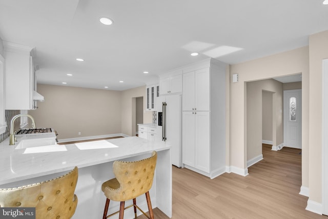 kitchen featuring a breakfast bar area, glass insert cabinets, white cabinetry, paneled fridge, and a peninsula