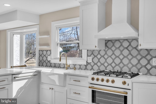 kitchen with a sink, white cabinetry, wall chimney range hood, dishwasher, and white gas range