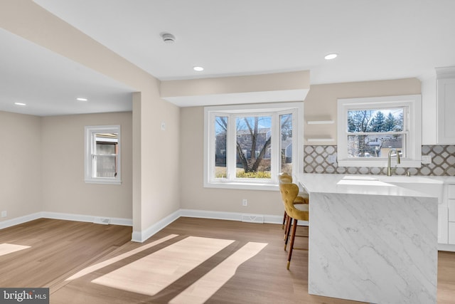 kitchen with light wood-style flooring, light stone counters, white cabinets, and decorative backsplash