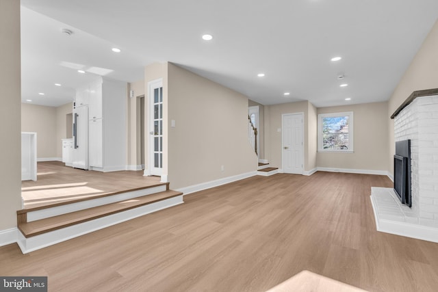 unfurnished living room with recessed lighting, a brick fireplace, light wood-style flooring, and stairs