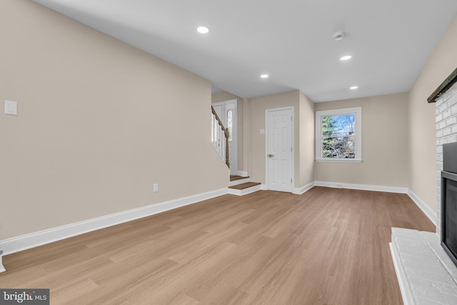 unfurnished living room featuring recessed lighting, baseboards, stairway, light wood-type flooring, and a brick fireplace