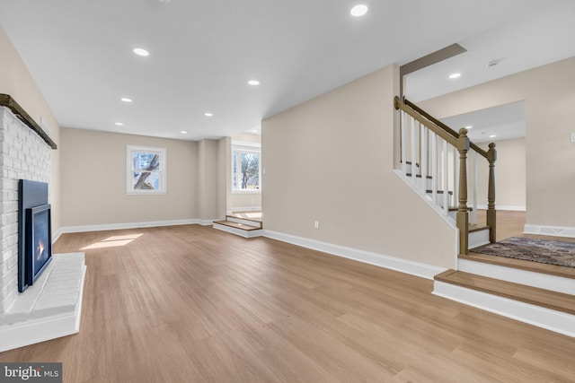 unfurnished living room with baseboards, stairway, wood finished floors, a brick fireplace, and recessed lighting