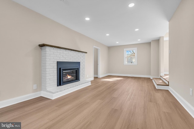 unfurnished living room featuring light wood-type flooring, recessed lighting, a brick fireplace, and baseboards