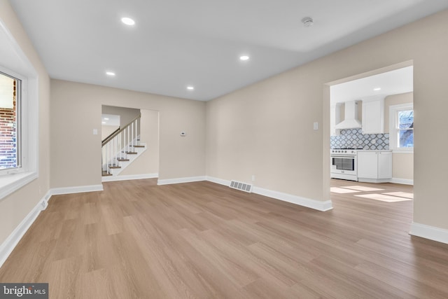 empty room featuring baseboards, stairway, visible vents, and light wood-style floors