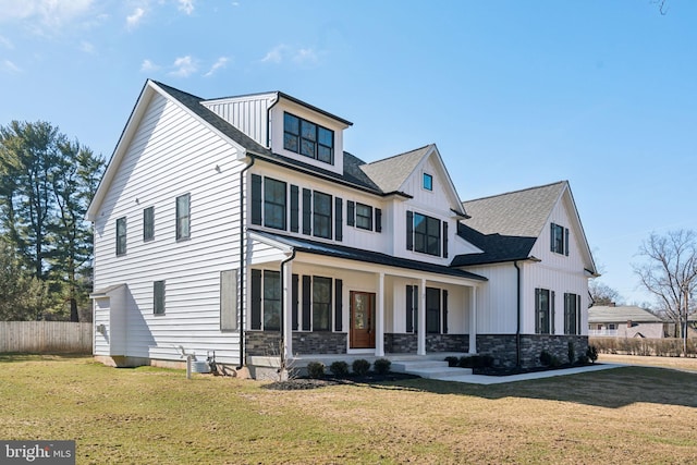 view of front facade featuring stone siding, a front yard, covered porch, and board and batten siding