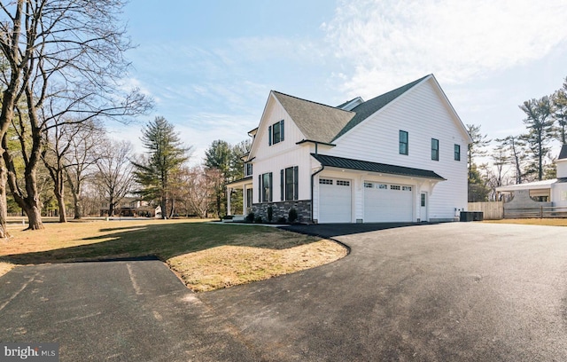 view of side of home with driveway, a lawn, an attached garage, a standing seam roof, and cooling unit