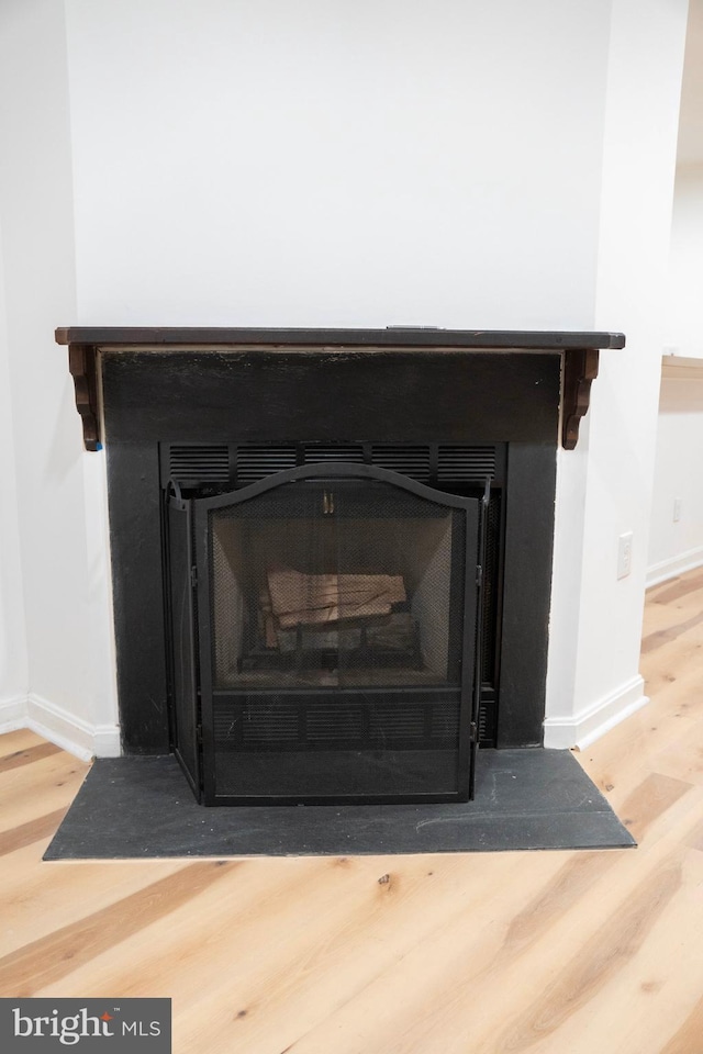 details featuring a fireplace with flush hearth, baseboards, and wood finished floors