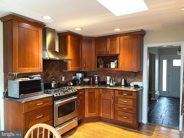 kitchen with stainless steel gas stove, dark stone countertops, wall chimney range hood, and a sink